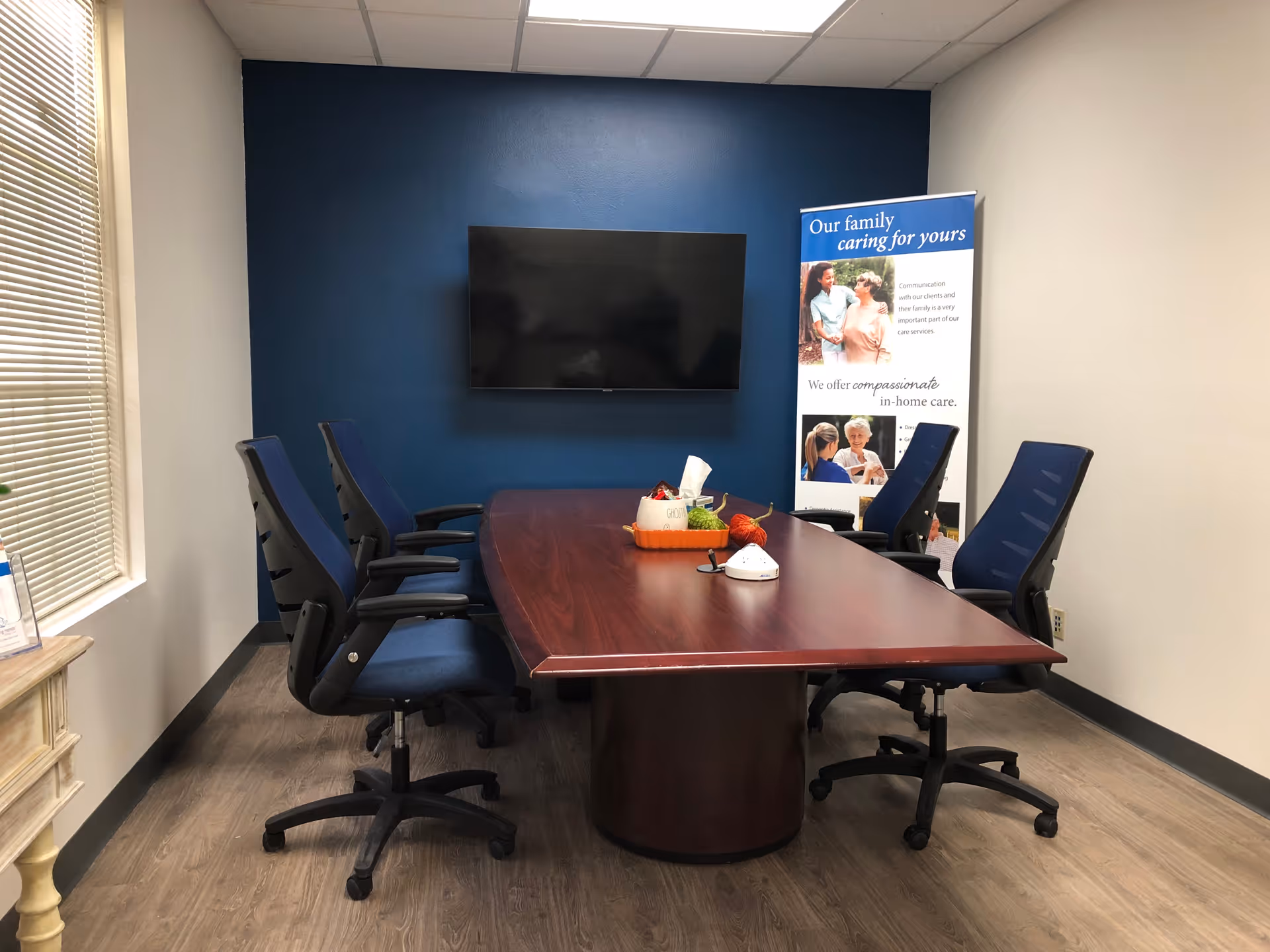 Conference room with a long table, blue chairs, TV, and banner.
