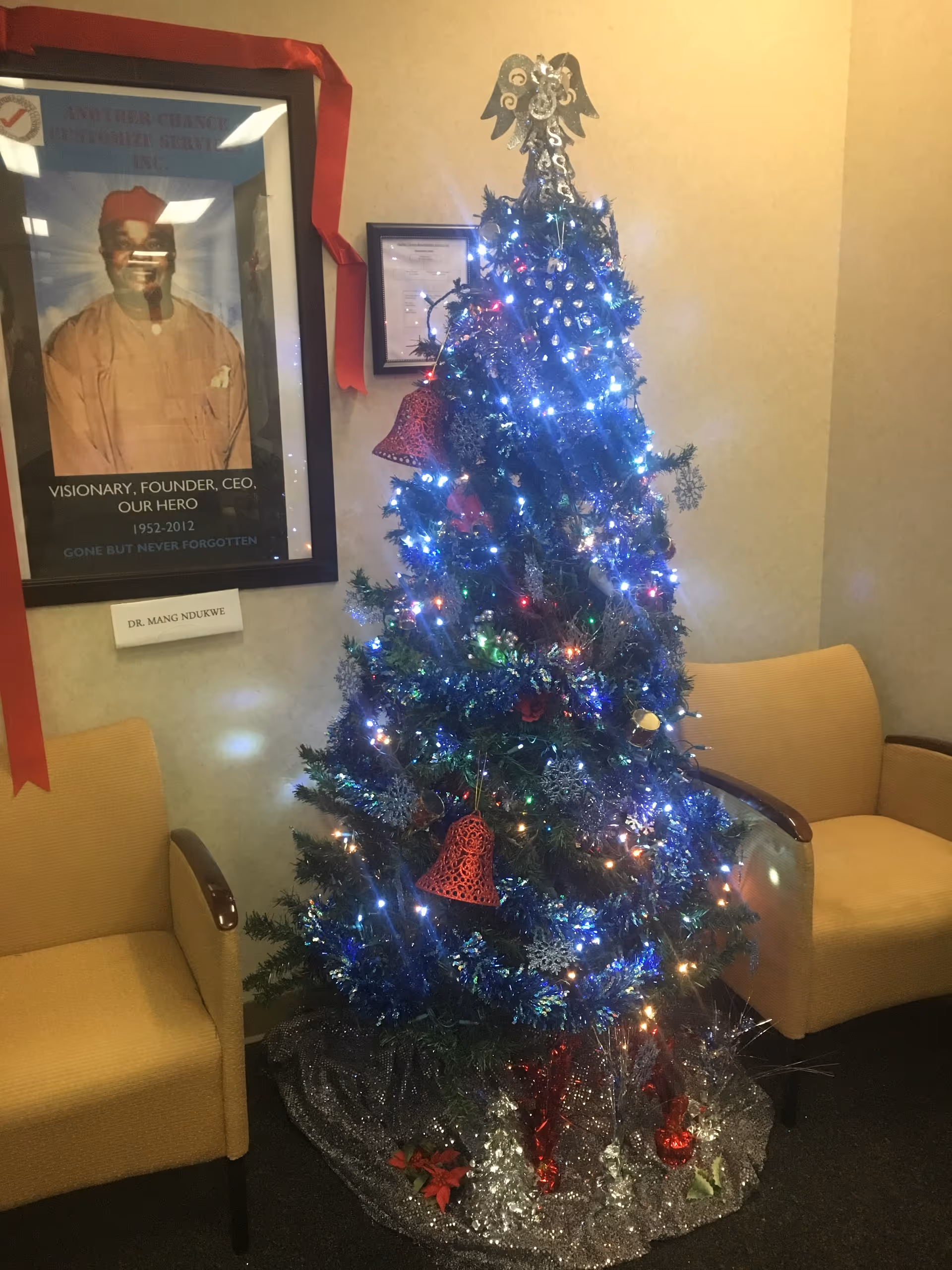 Decorated Christmas tree with blue lights sits between two beige armchairs in a hallway.