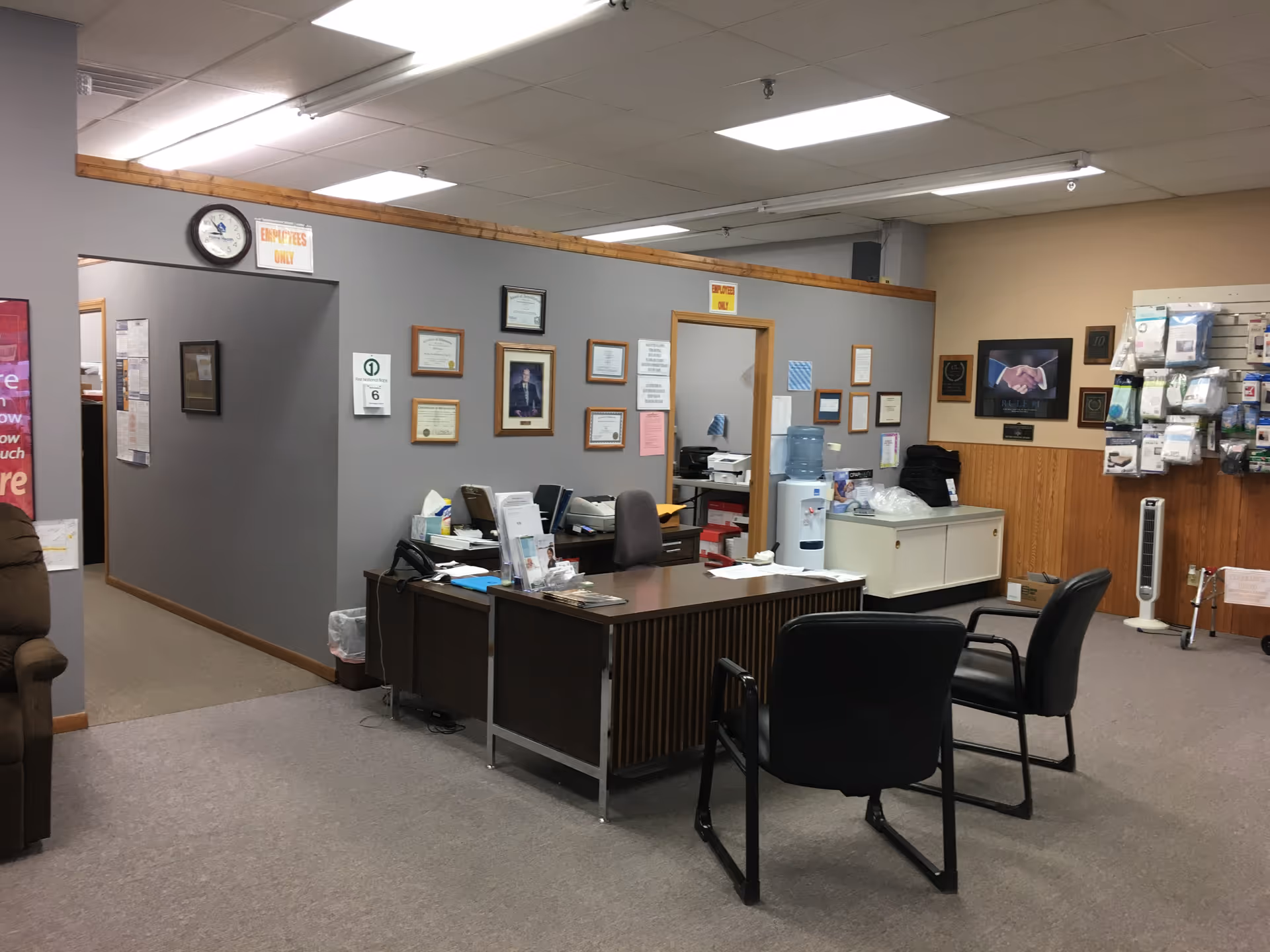 Reception desk with certificates on the wall, chairs, and office equipment in a medical lobby.