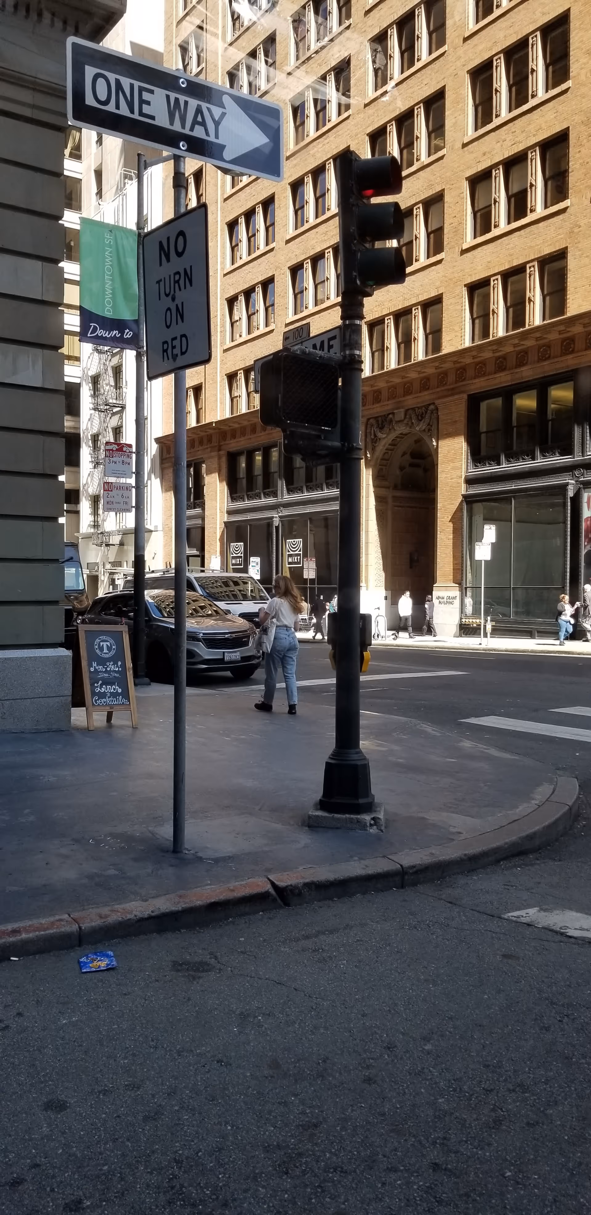 Urban street scene with crosswalk, traffic signals, and pedestrians beside tall brick buildings.
