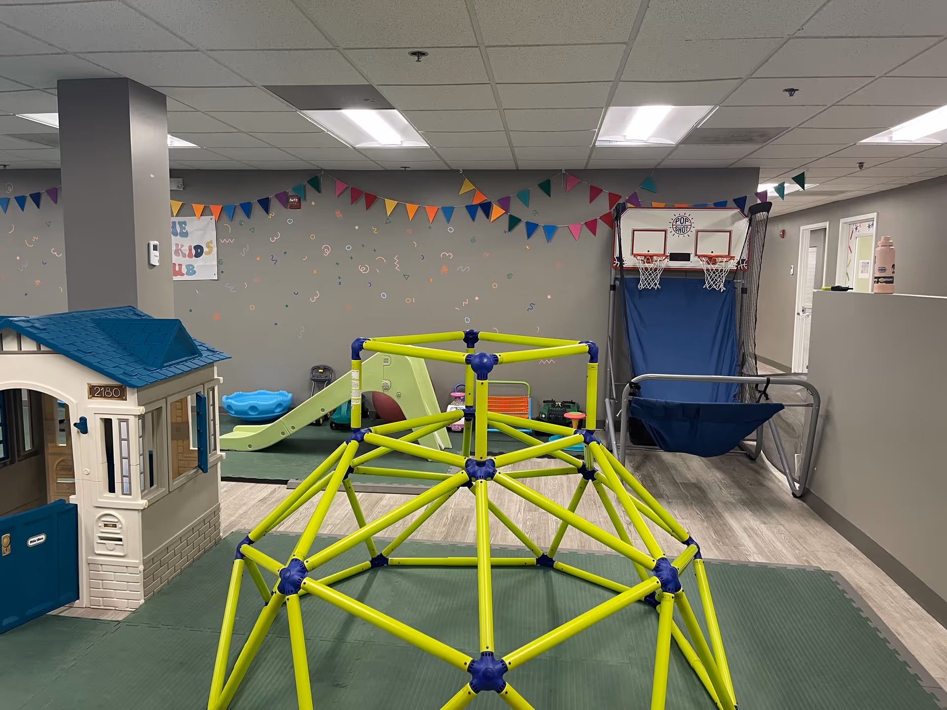 Indoor children's play area with bright climbing frame, playhouse, and swing.