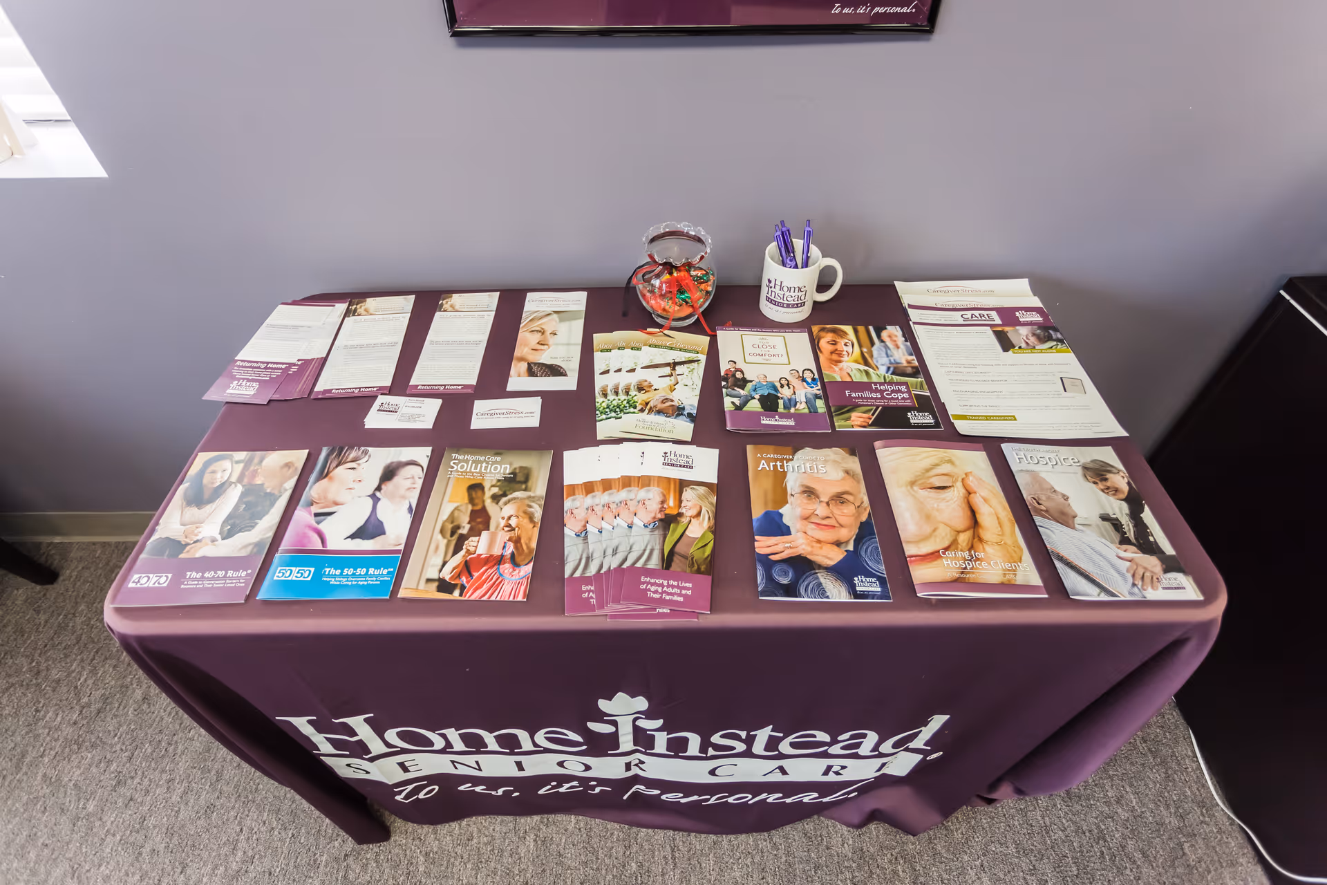 A purple branded Home Instead table with brochures and a mug on a promotional display.