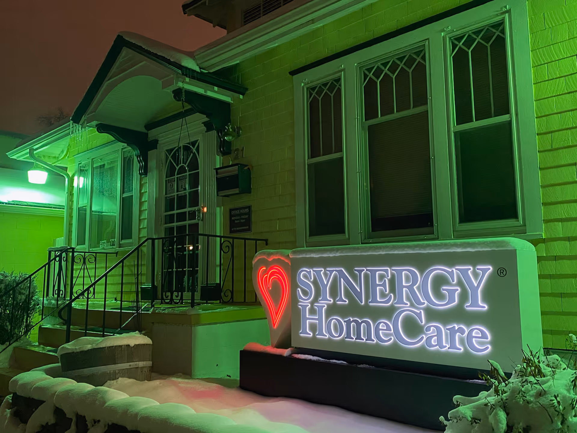 Night exterior of SYNERGY HomeCare building with illuminated sign and snowy steps.