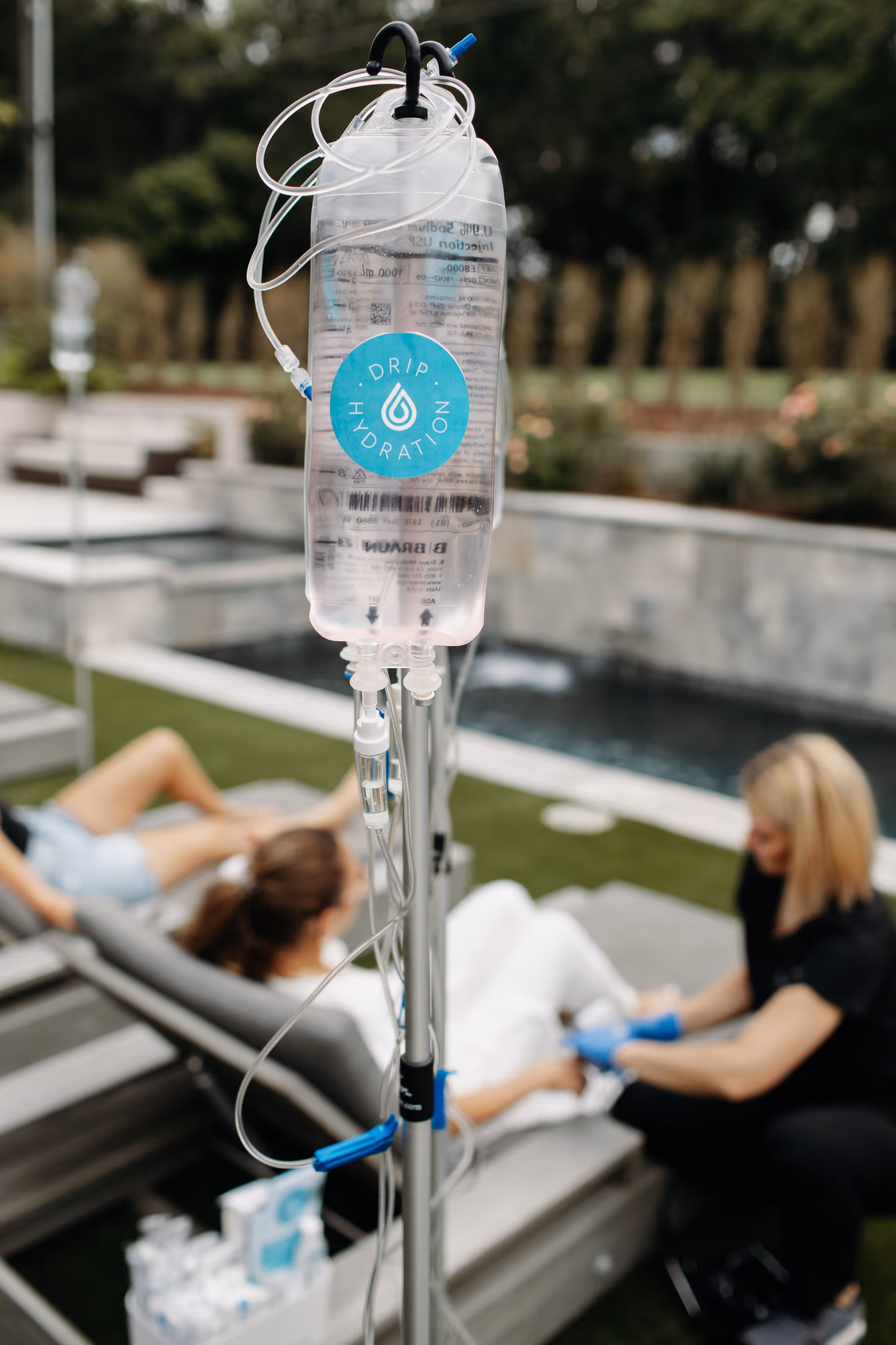 IV infusion bag on a pole outdoors while a caregiver tends a resident near lounge chairs