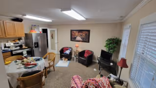 Open-plan kitchen and living area in a senior facility with table, chairs, and plants.