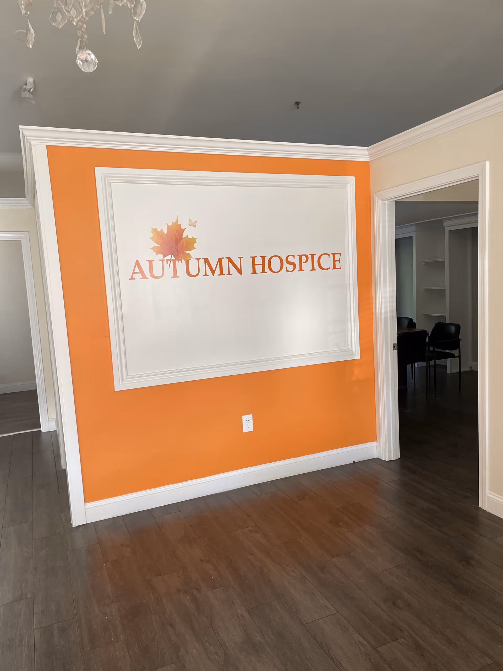 Orange-walled interior hallway featuring a large Autumn Hospice sign in a white framed panel.