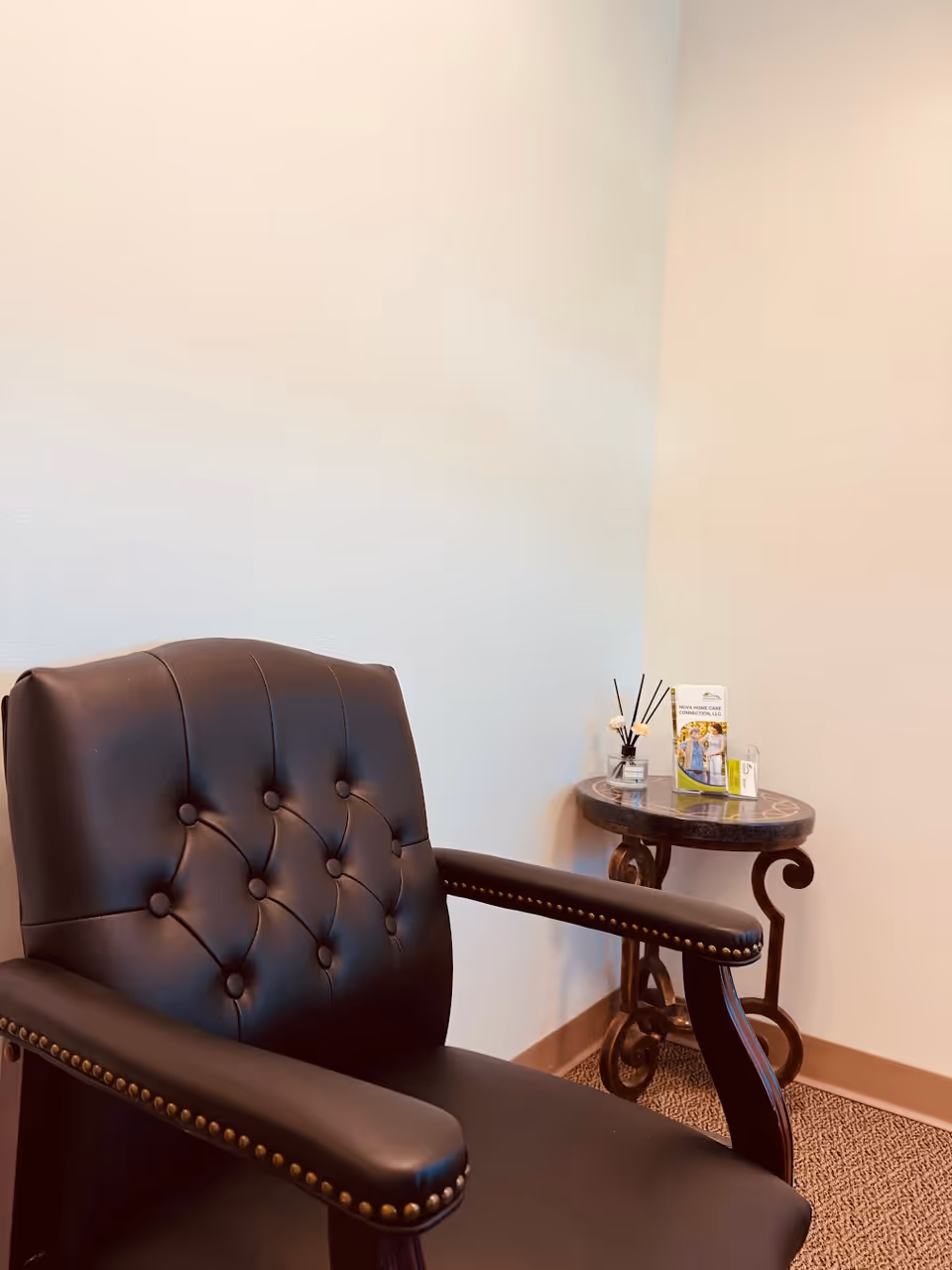 Black tufted leather chair beside a round side table with brochures in a lobby.