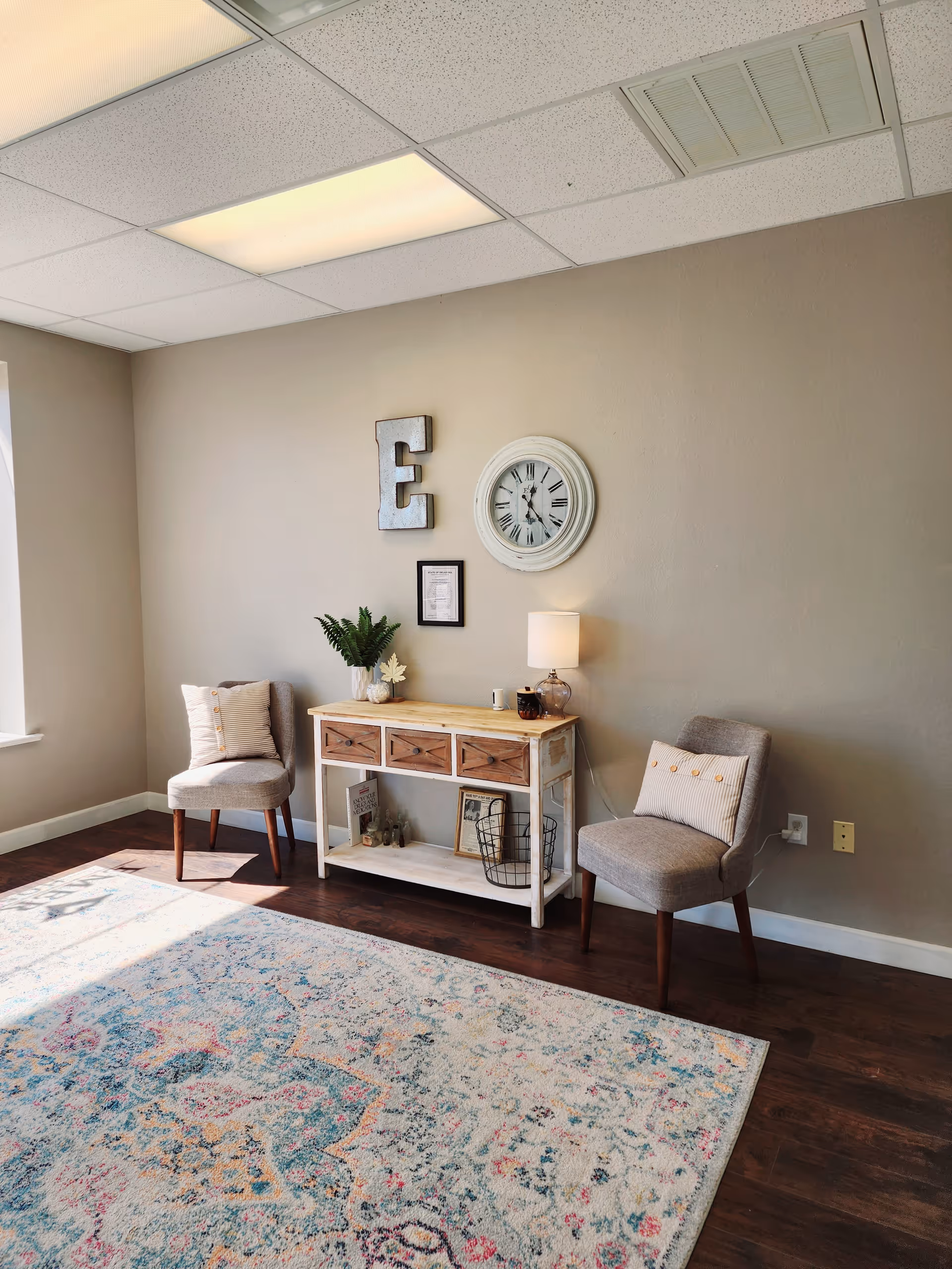 A cozy living area with two chairs, a console table, plant, and wall clock.