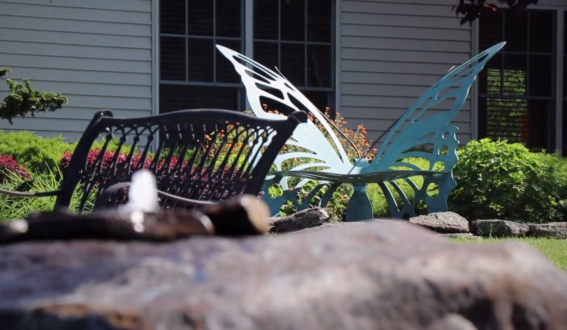 Front garden area with a butterfly sculpture and metal chair outside a building.