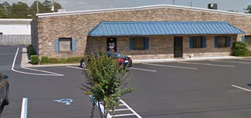 Brick facility with a blue awning, parking lot, and a few trees in front.