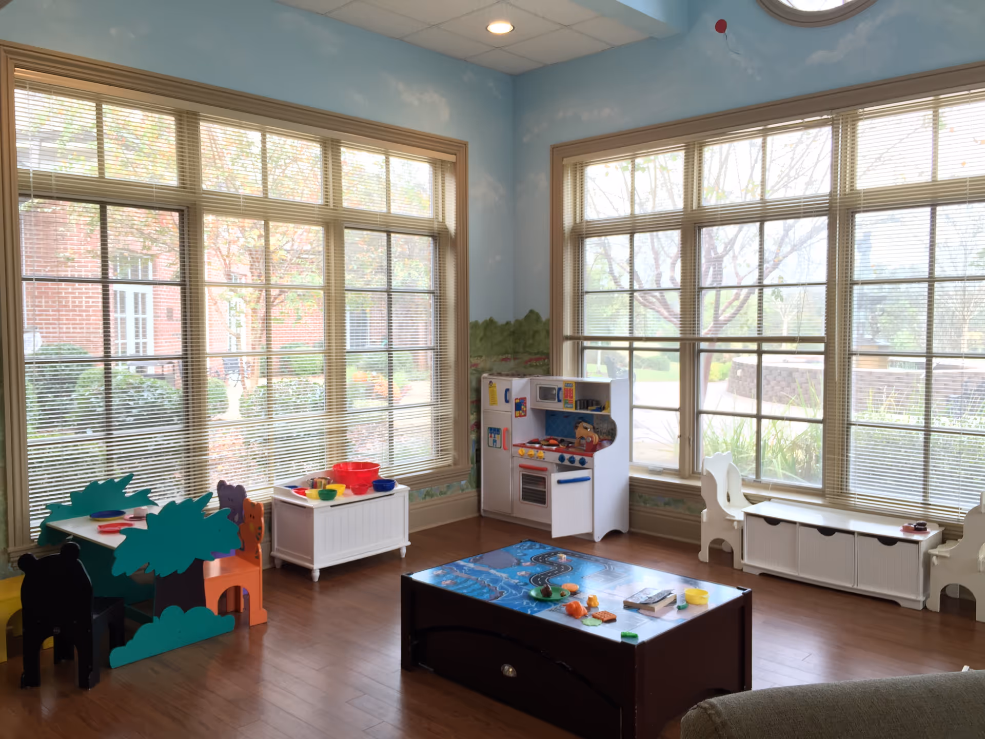 Bright children's play area with toy kitchen, tables, and large windows.
