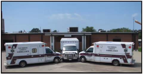Three ambulances marked Van Buren County Hospital are parked in front of a brick, sunlit building.