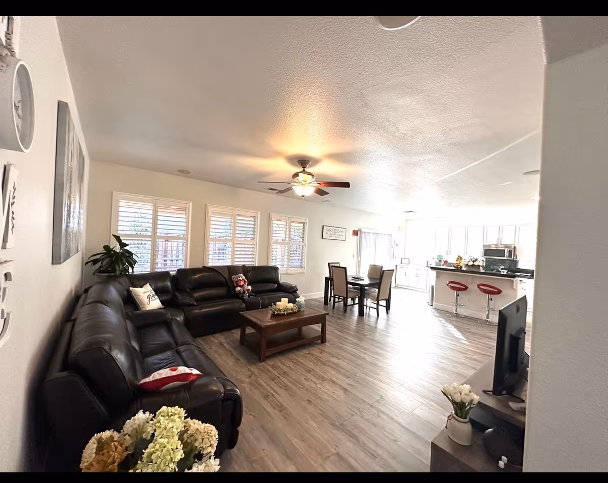 Open-concept living room with a black leather sectional, coffee table, dining area, and bright kitchen.