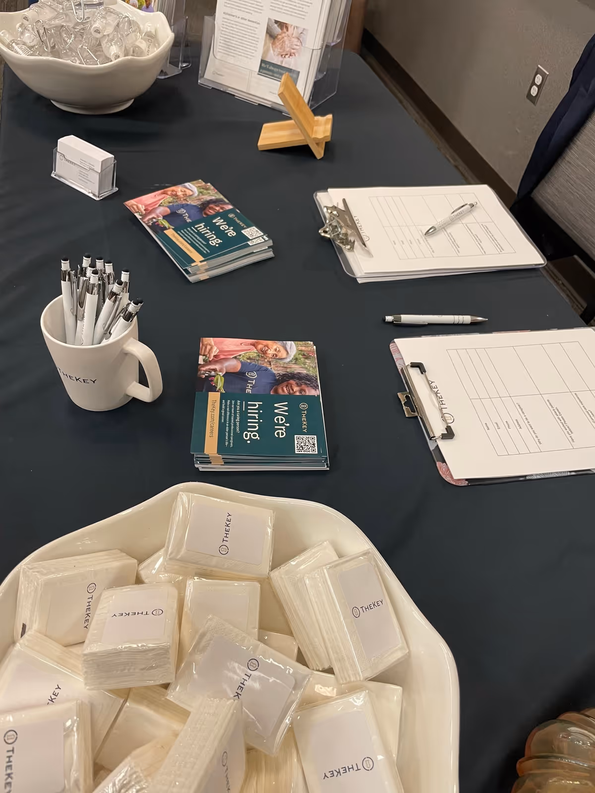 Indoors, a promotional table displays TheKey senior care brochures, pens, and clipboards.
