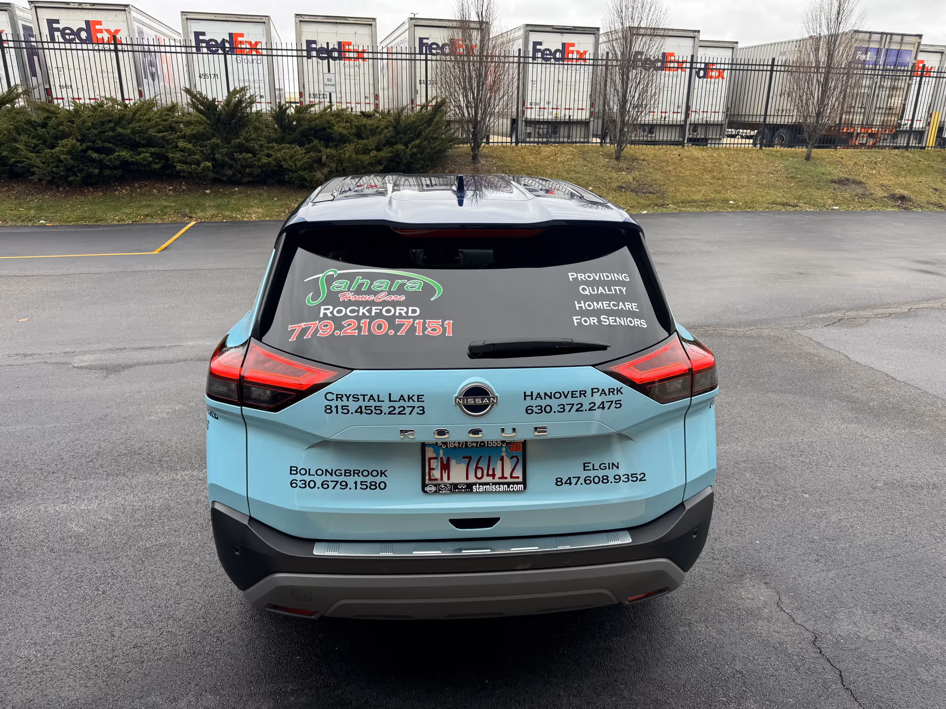 Rear view of light blue Sahara Home Care van parked in a lot with FedEx trailers