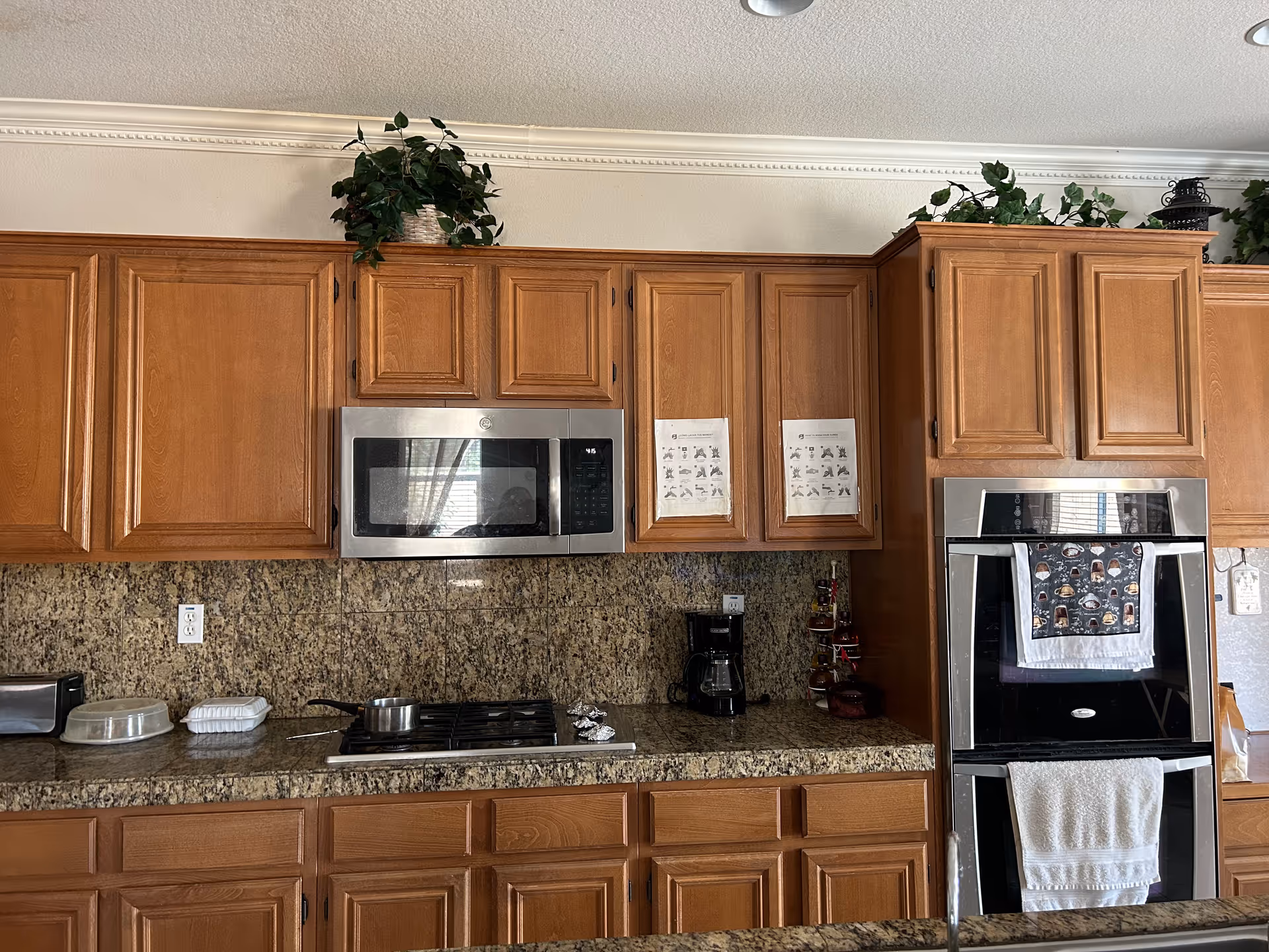 Wooden kitchen cabinets with granite countertops, microwave, stove, oven, and coffee station.