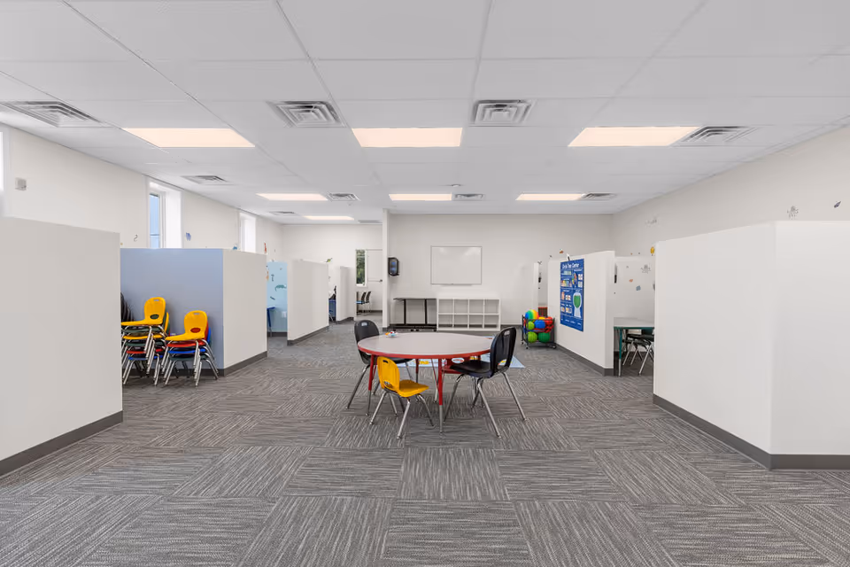 Bright open interior with partitioned cubicles, a round table, and colorful chairs.
