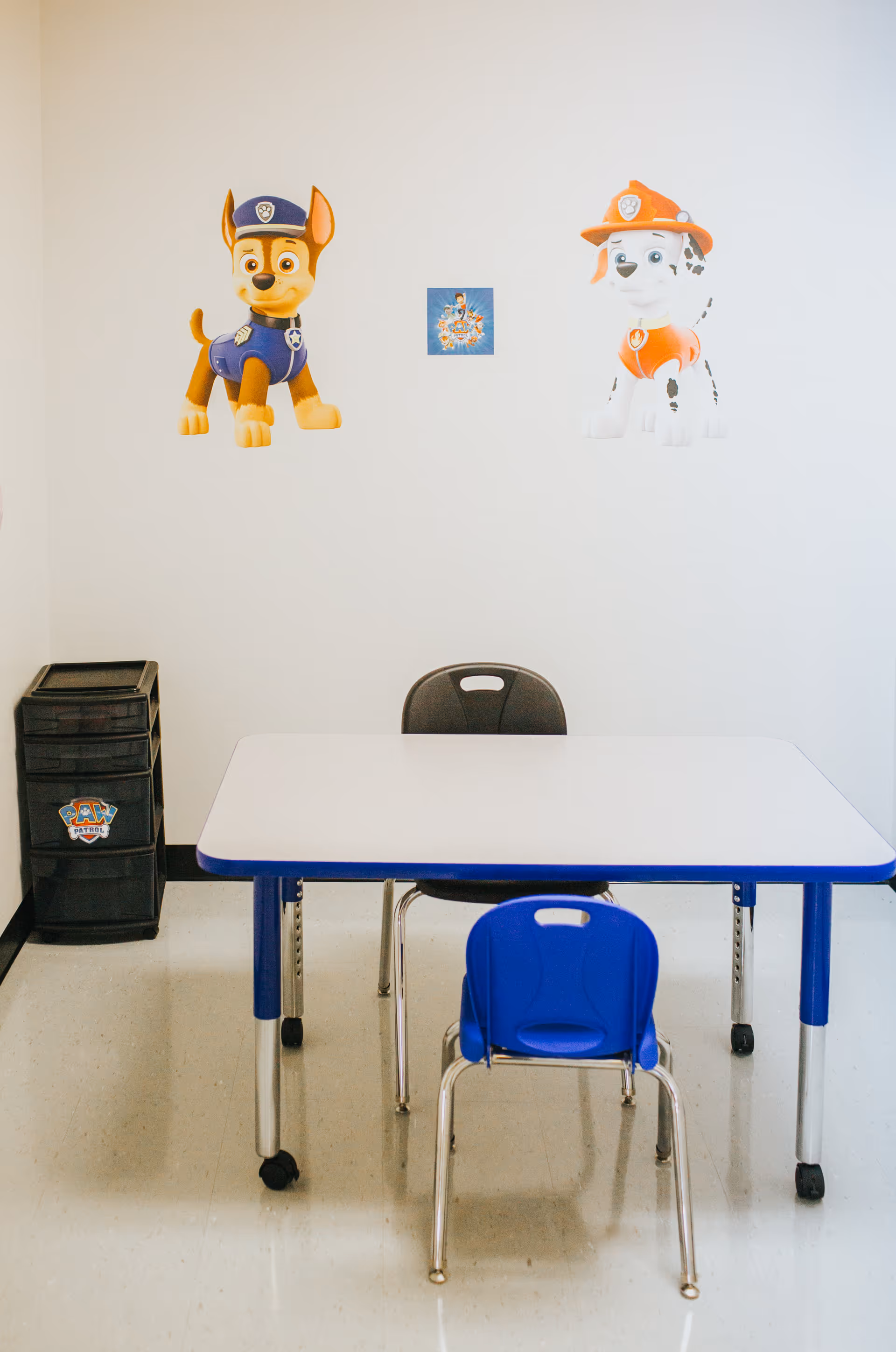 Therapy play area with a white table, blue chairs, and Paw Patrol decals.