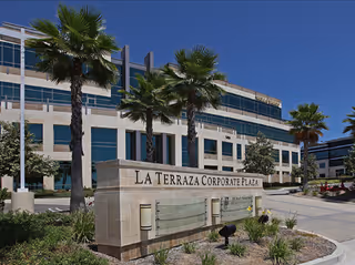 Exterior view of a modern building with palm trees and a La Terraza Corporate Plaza sign.