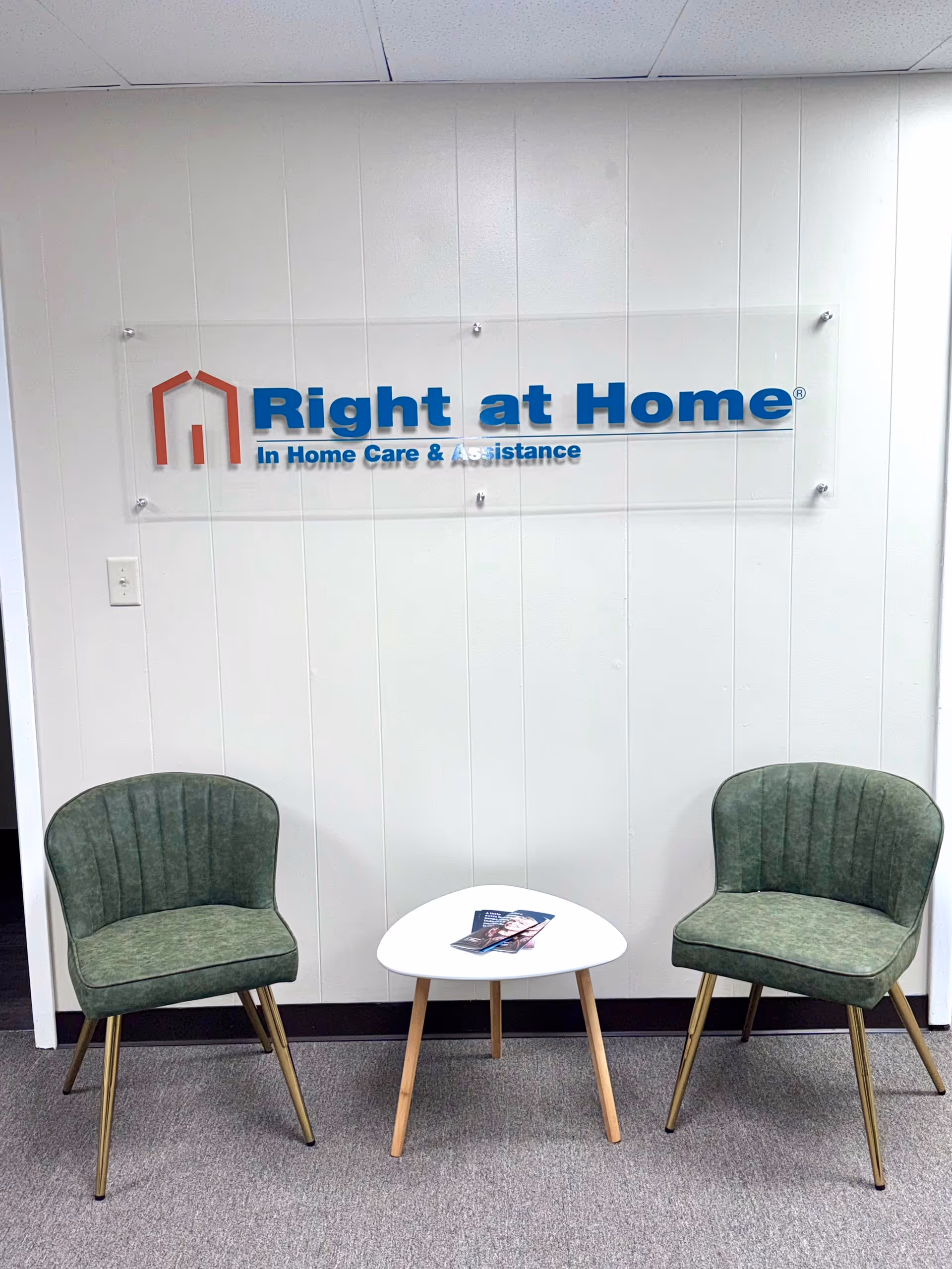 Lobby seating with two green chairs and a small white table near Right at Home sign