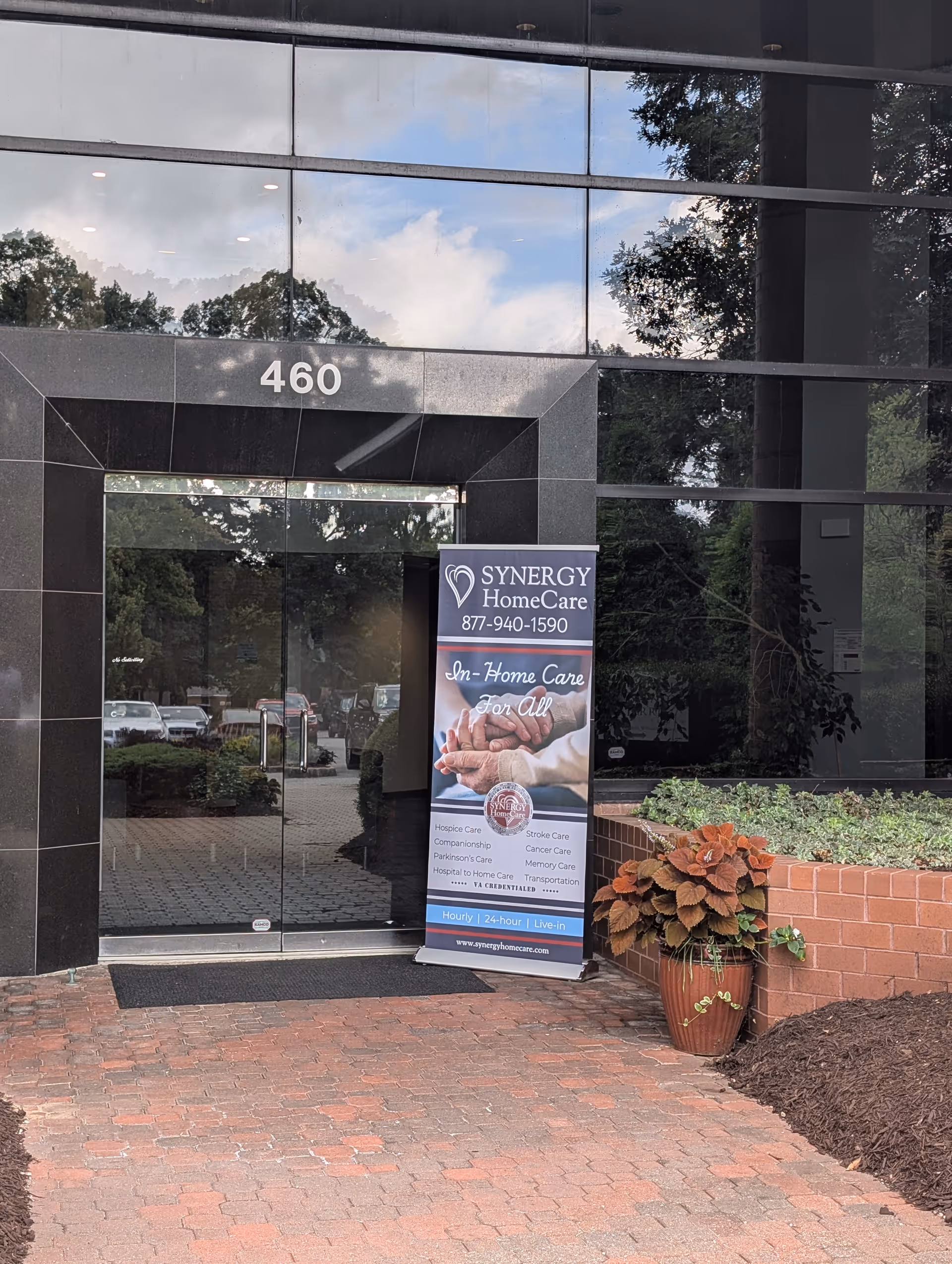 Modern glass-front entrance with Synergy HomeCare banner and potted shrubs near 460.