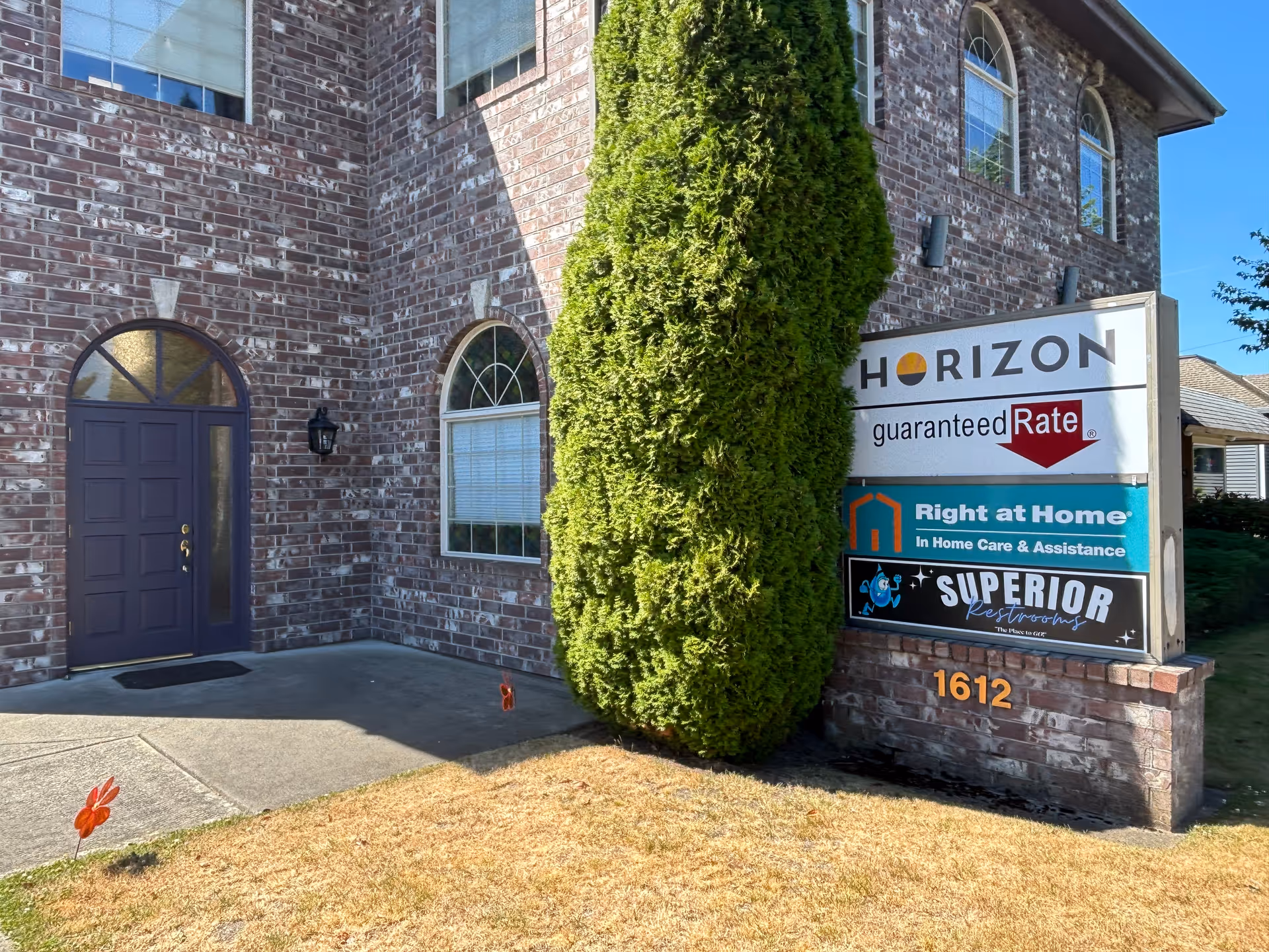 Brick building exterior with a purple door, shrub, and signs for Horizon and Right at Home.