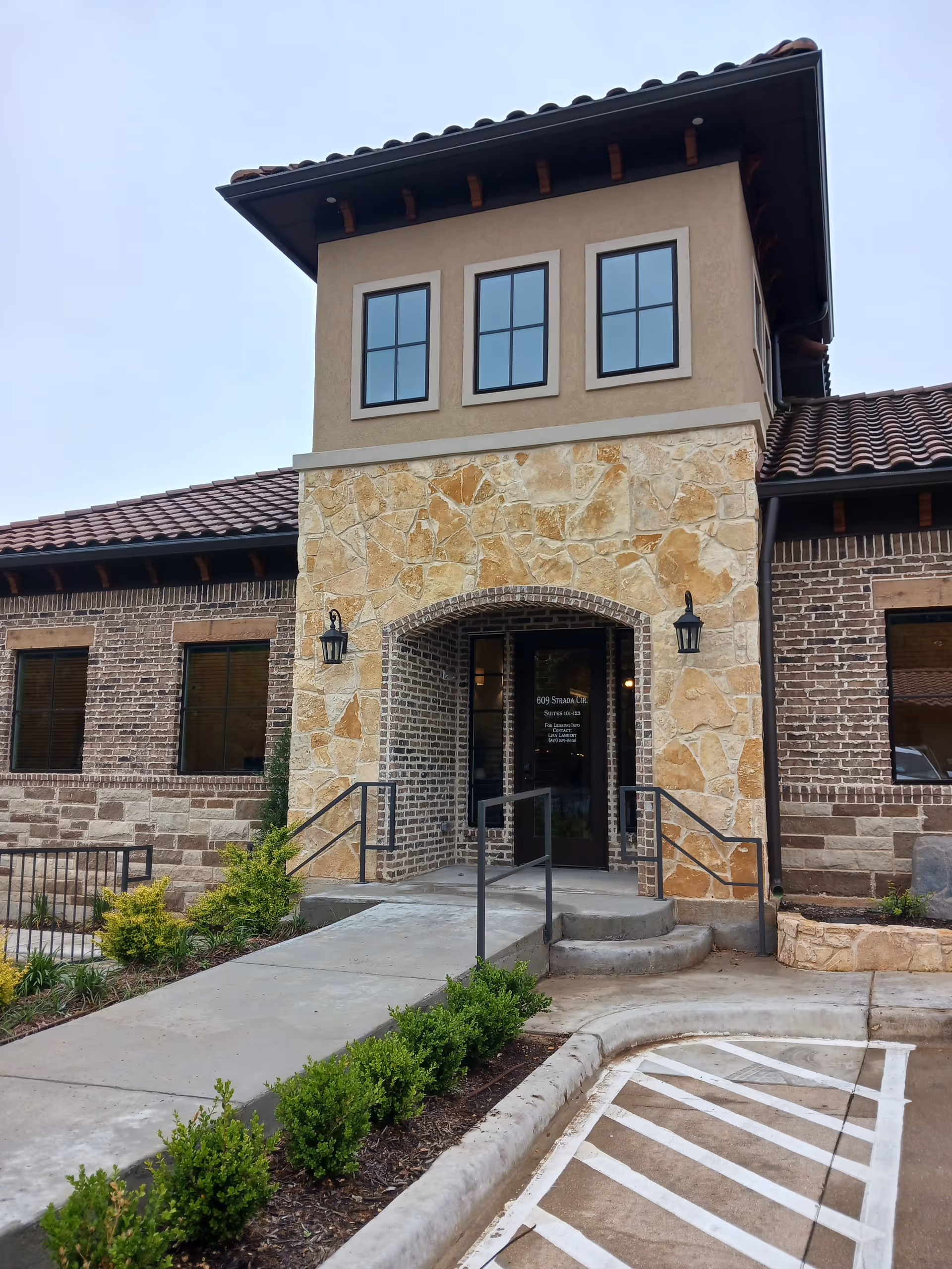 Stone-front entrance with arched doorway, brick walls, and landscaped walkway.
