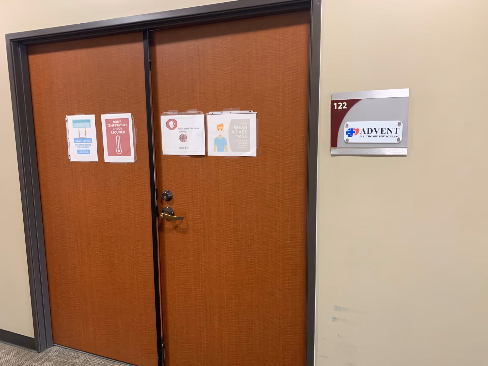 Two wooden doors in a beige hallway with Advent Healthcare Services, Inc. signage.