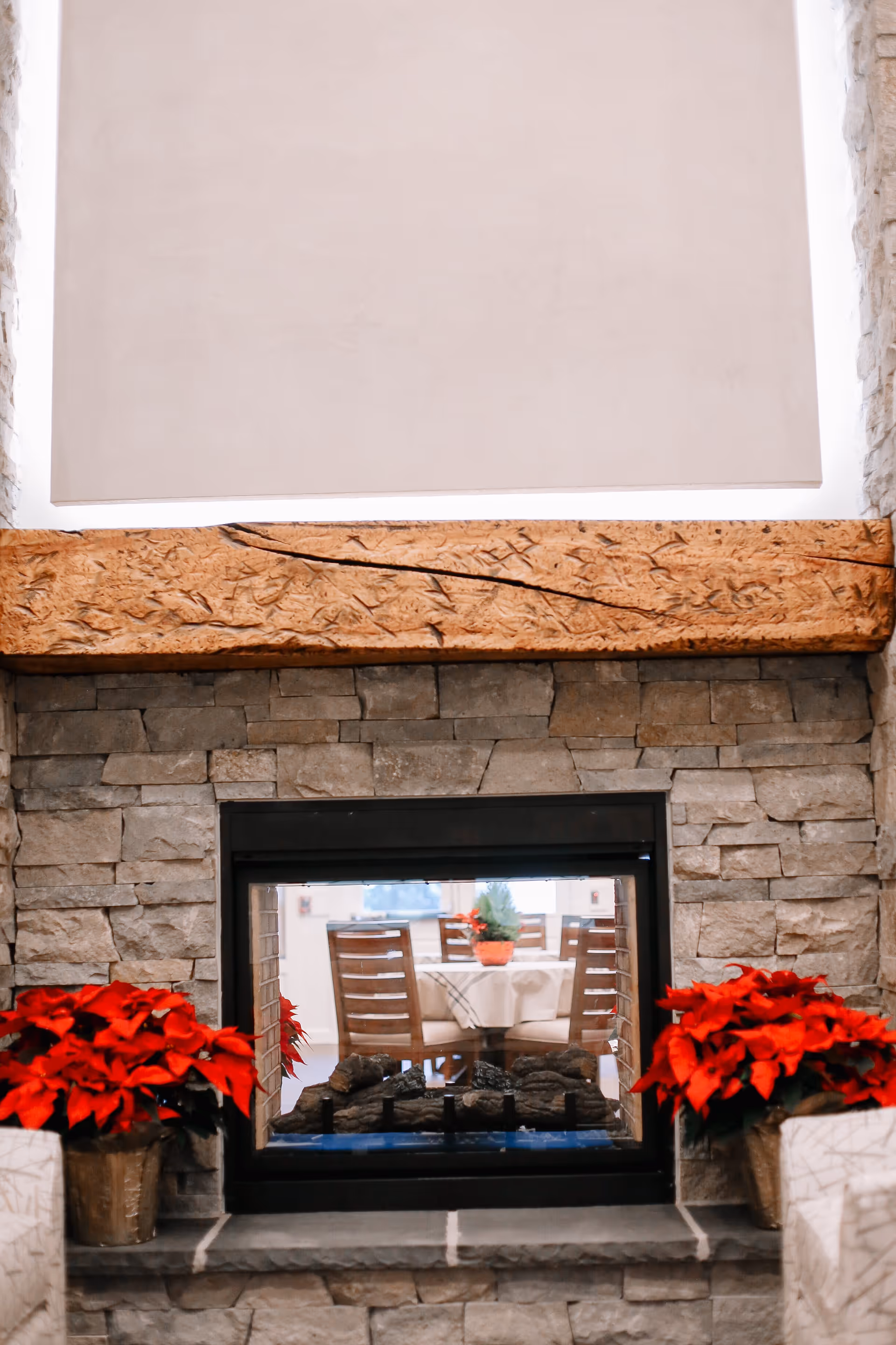 Stone fireplace with a viewing window and red poinsettias beside a dining area.