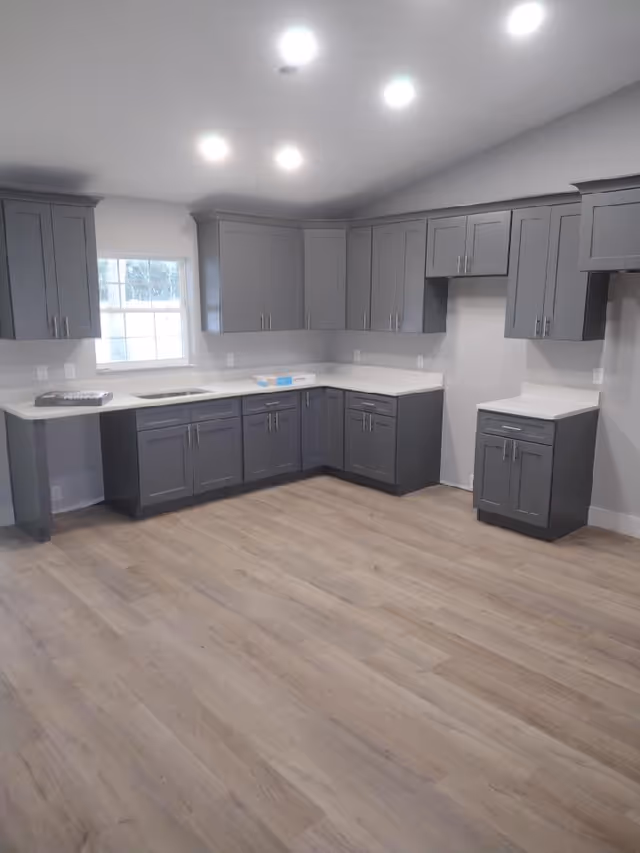 Grey kitchen cabinets with white countertops create a spacious, empty kitchen.