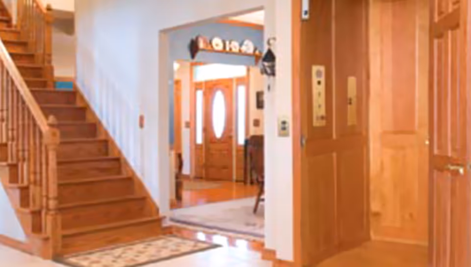 Interior hallway with wooden stairs and elevator doors in a senior living facility.