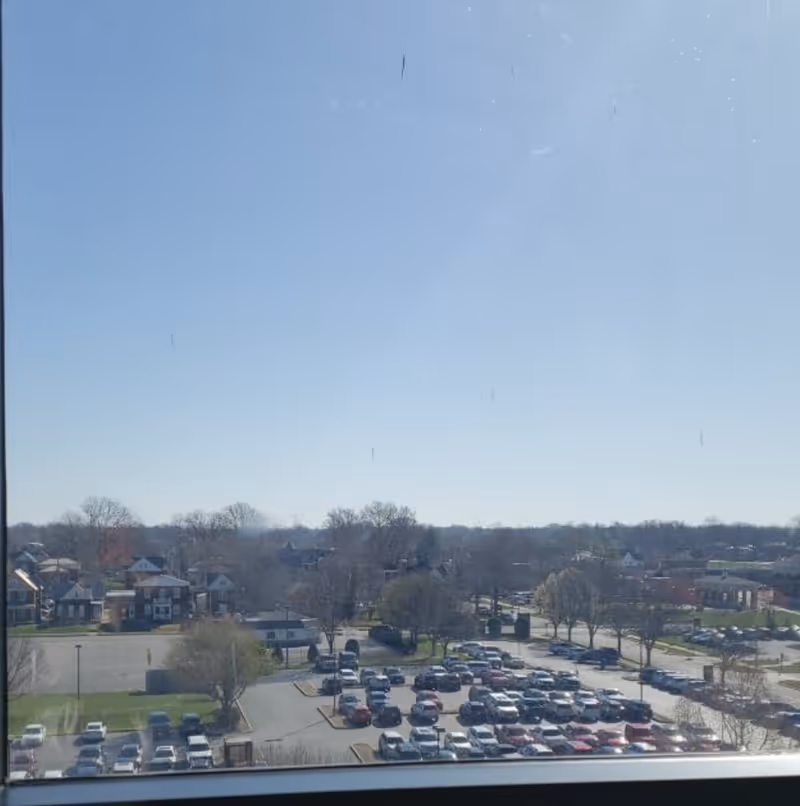 View through a window of a parking lot and distant houses under clear blue sky.