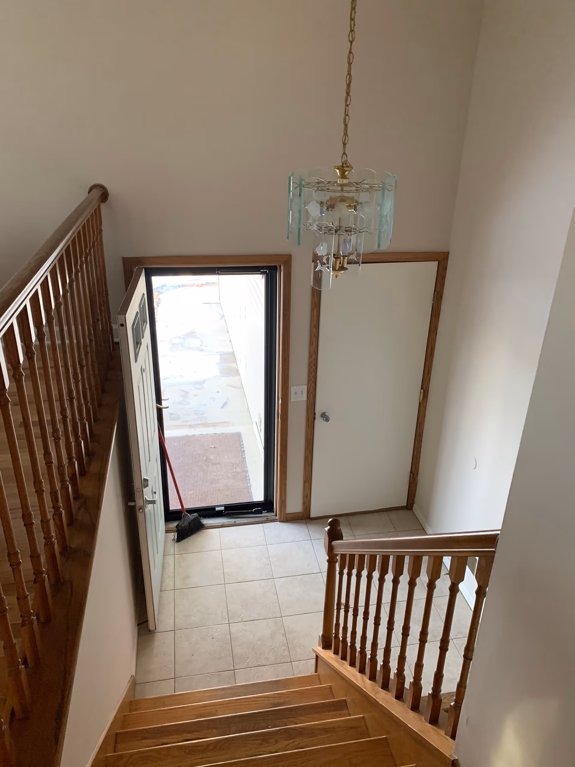 Interior foyer with staircase, chandelier, and open front door to outside.