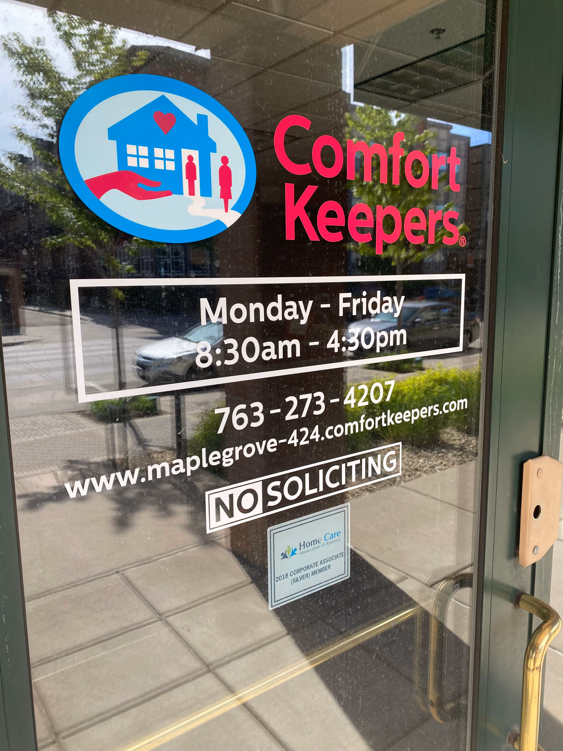 Glass door with Comfort Keepers logo, hours, phone number, website, and No Soliciting sign.