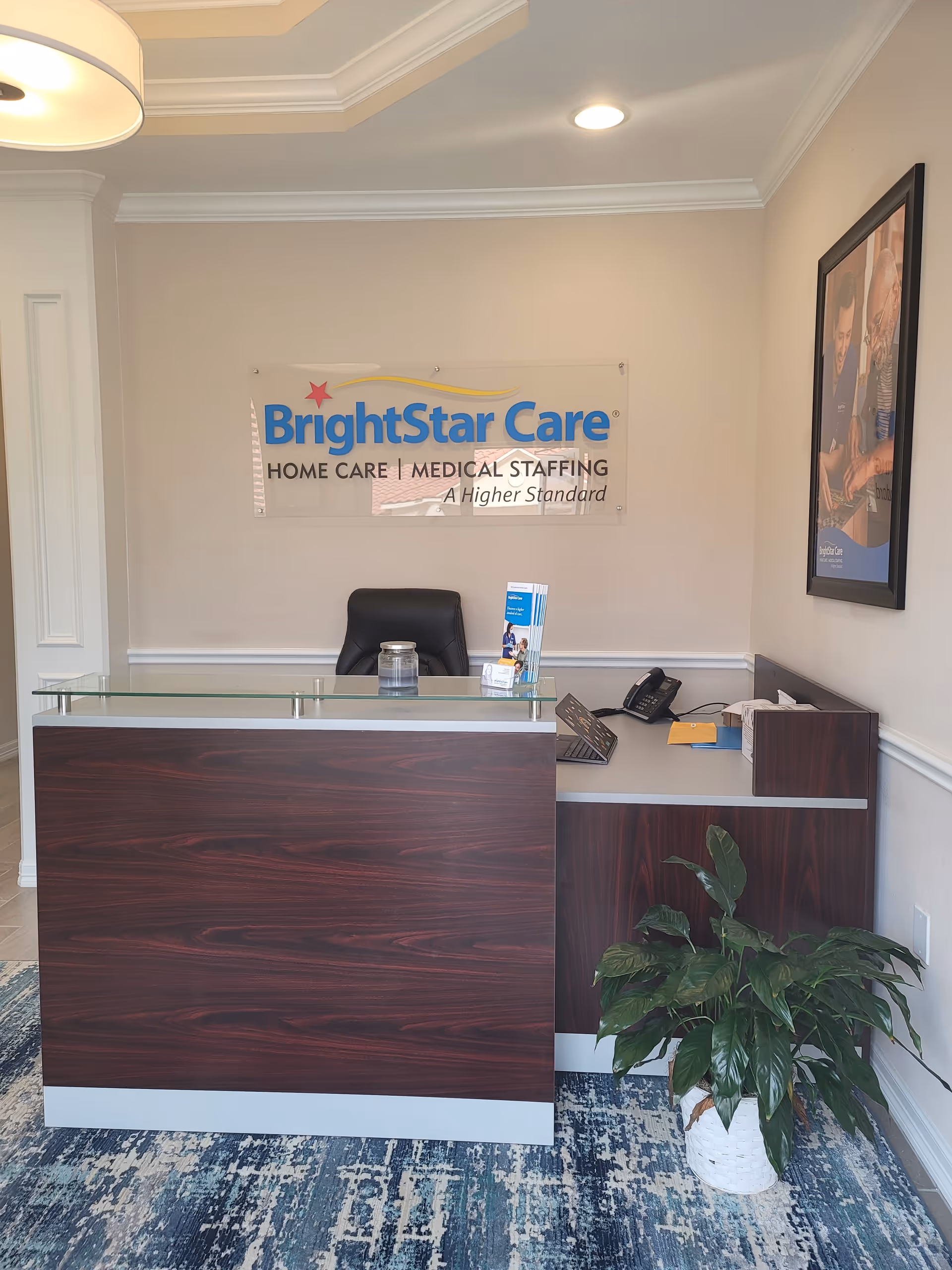 A reception desk in BrightStar Care lobby with a sign, phone, brochures, and a plant.