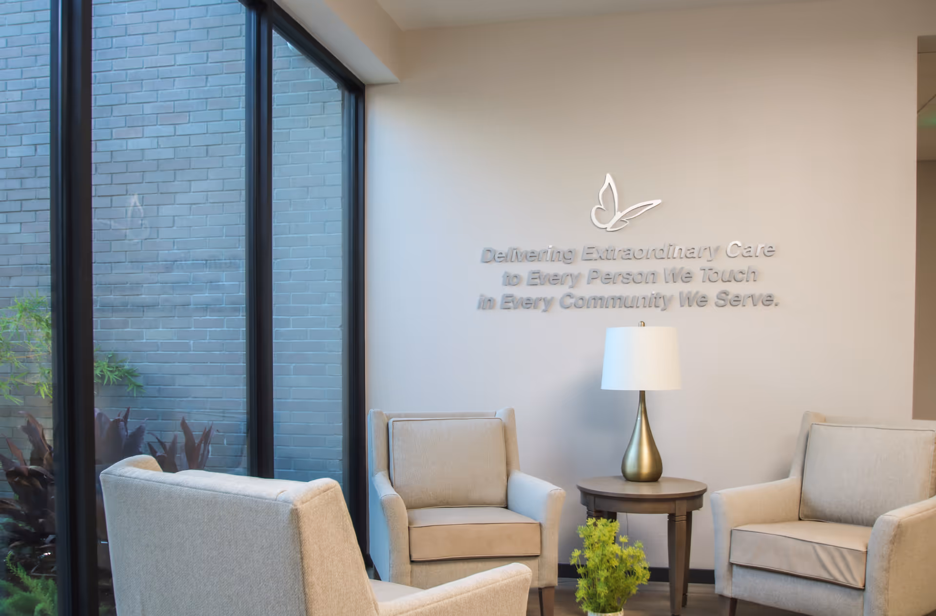 A cozy lounge area with beige armchairs, a round table, lamp, and wall text.