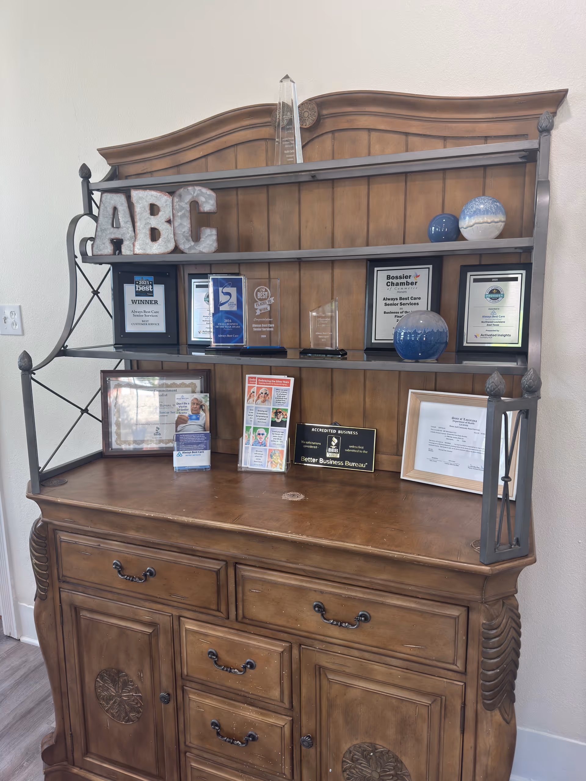 A wooden hutch with shelves displaying numerous awards in an interior setting.