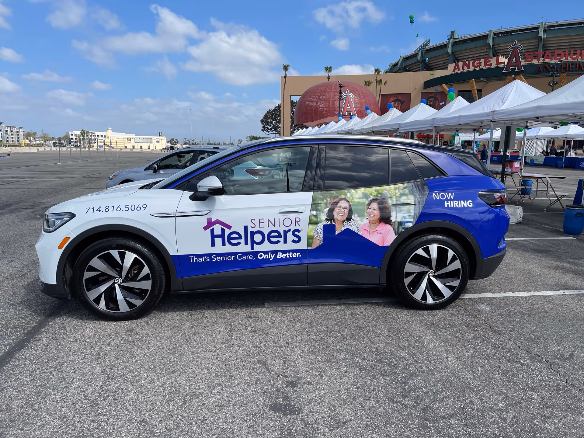 Senior Helpers branded car parked in a parking lot near tents and a stadium.