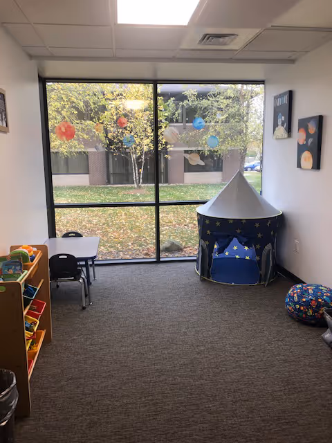 Interior playroom with a small tent, child sized table and chairs, and toy shelves.
