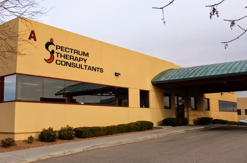 Yellow Spectrum Therapy Consultants building exterior with large sign and green awning.