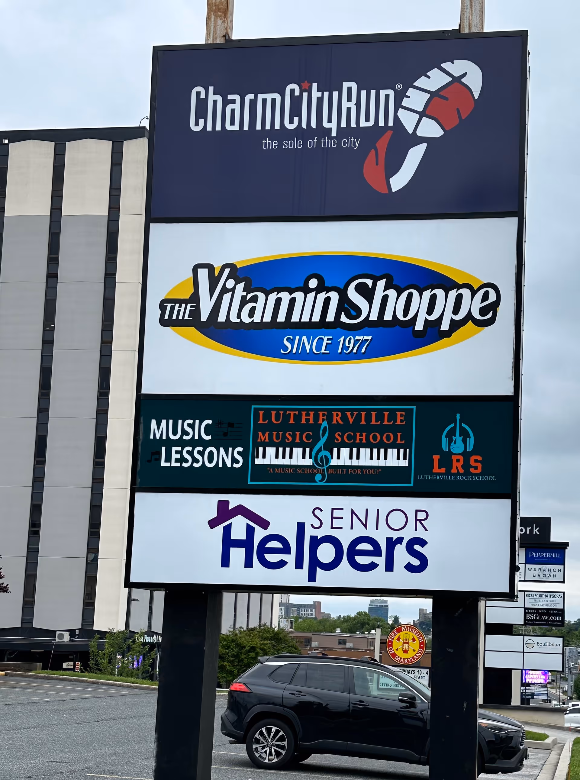 Tall outdoor sign with multiple business signs, including Senior Helpers, near a parking lot.