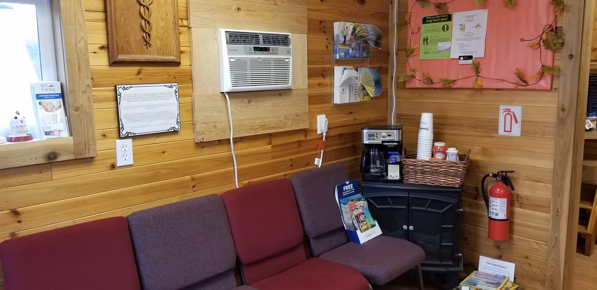 Wood-paneled lounge with maroon chairs, a coffee station, and a fire extinguisher.