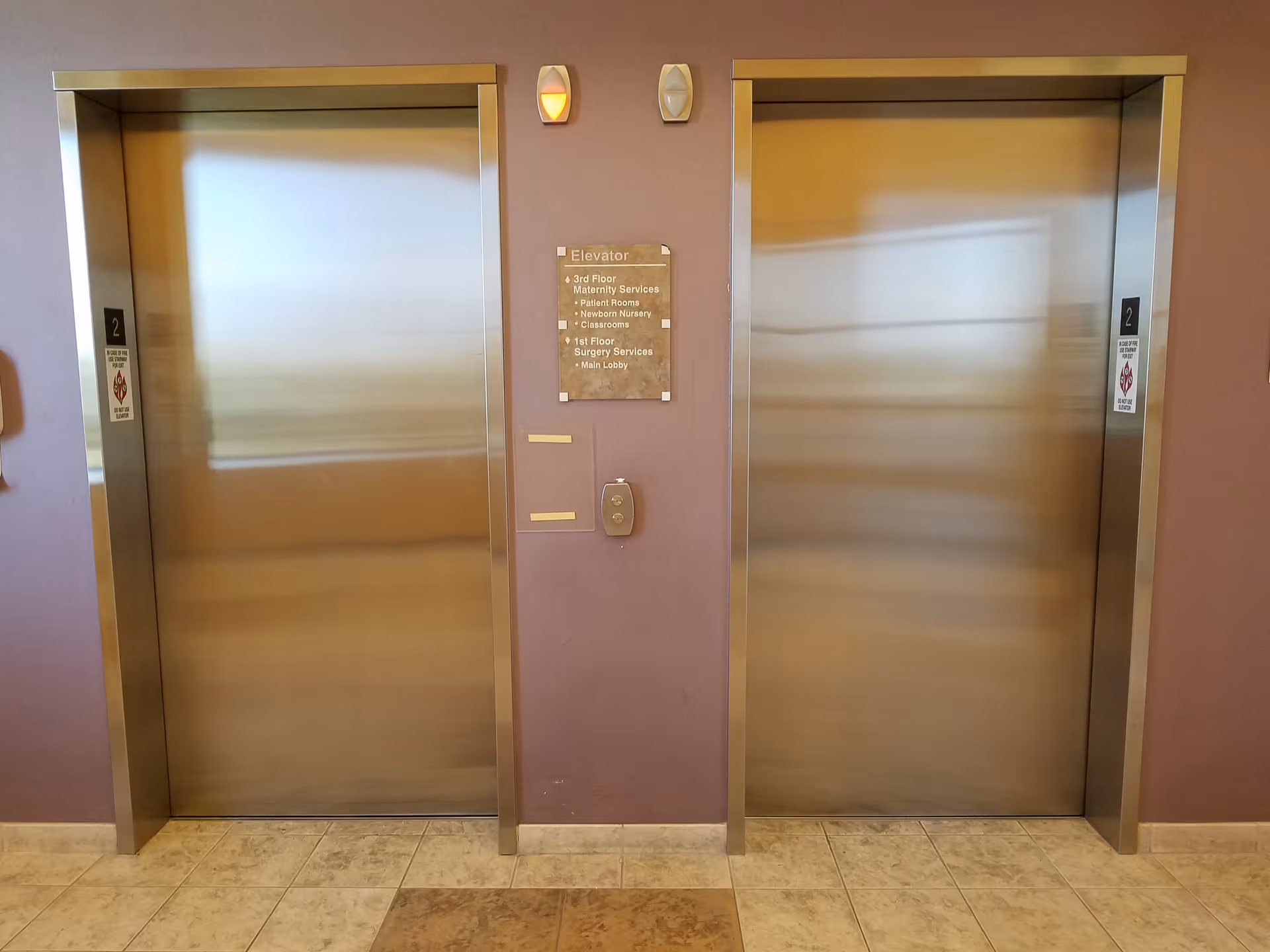 Two stainless steel elevator doors in a purple-walled hallway with tiled floor.