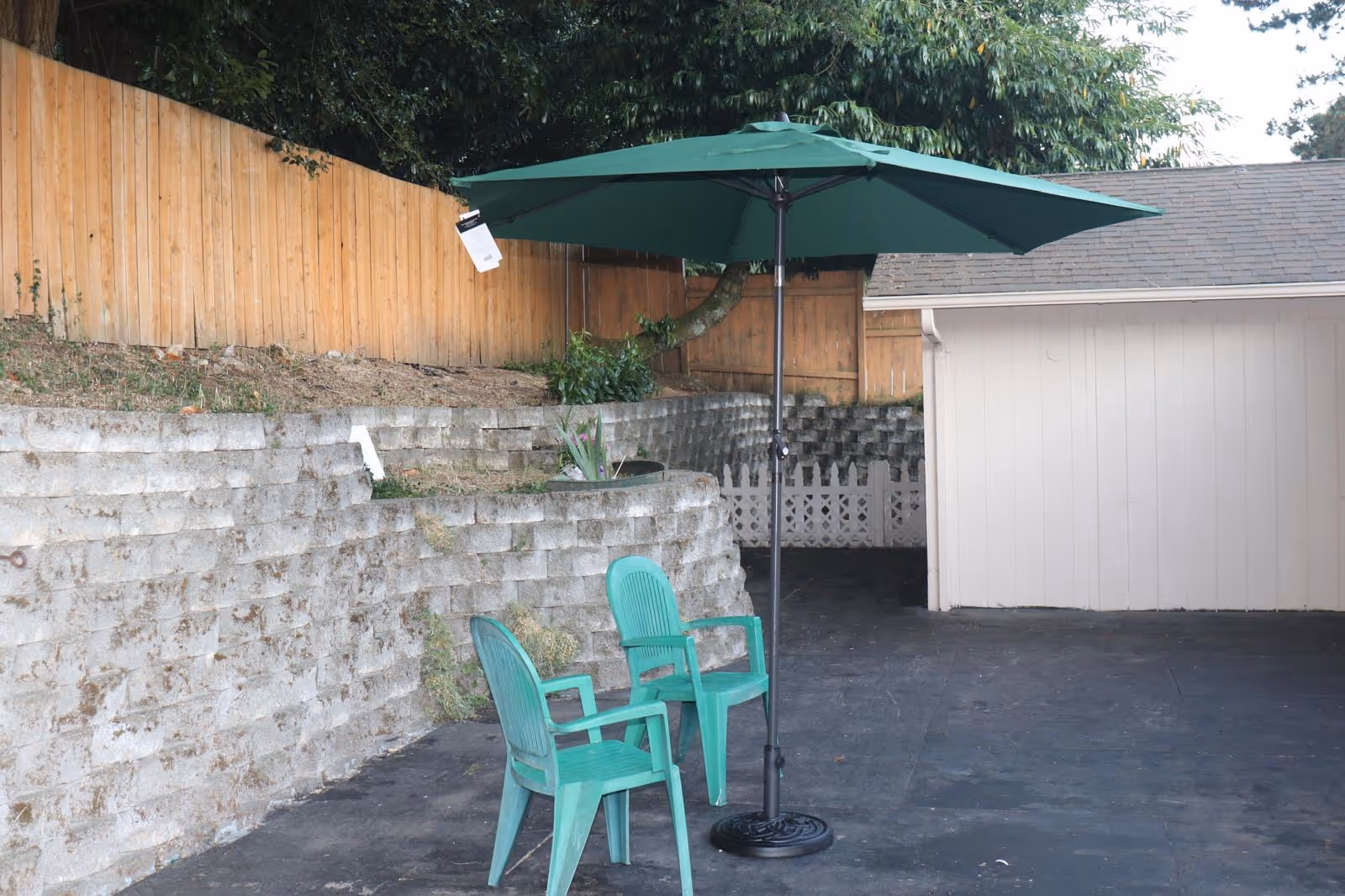 Two green plastic chairs under a large umbrella beside a retaining wall.