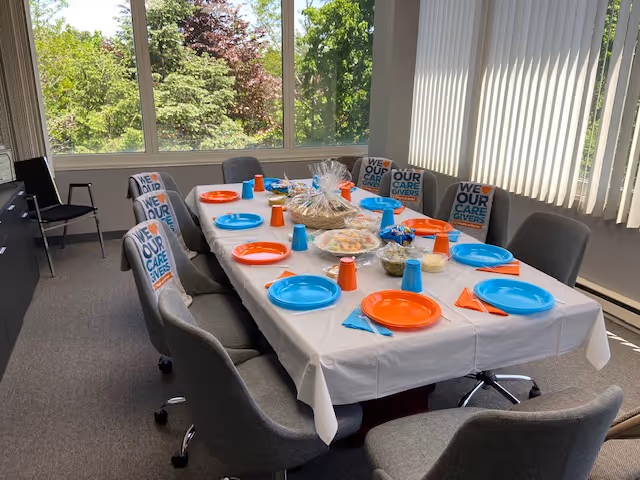 Empty chairs surround a long dining table set with colorful plates in a bright room.
