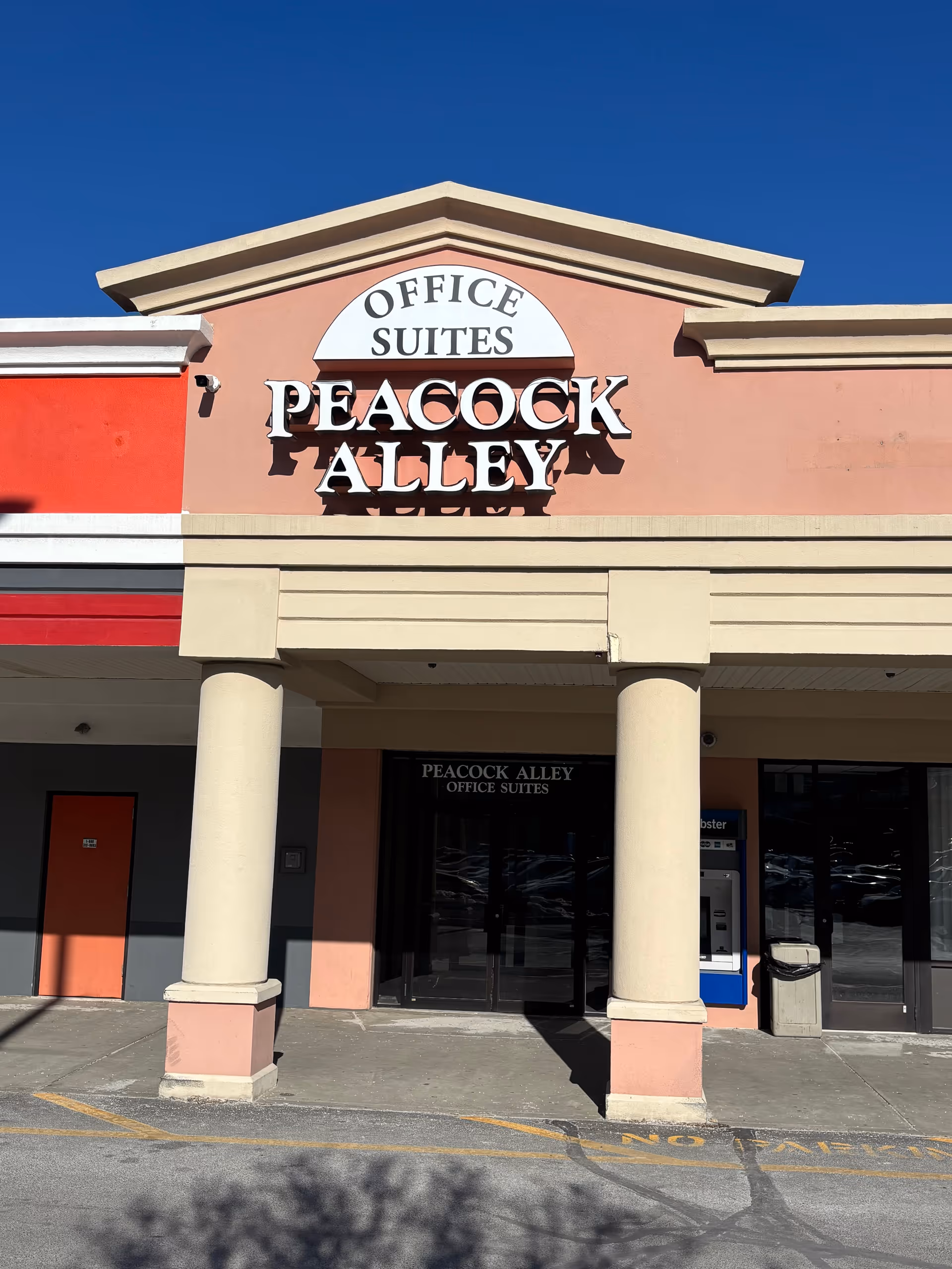 Exterior storefront with pink-beige facade, columns, and Peacock Alley office suites signage.