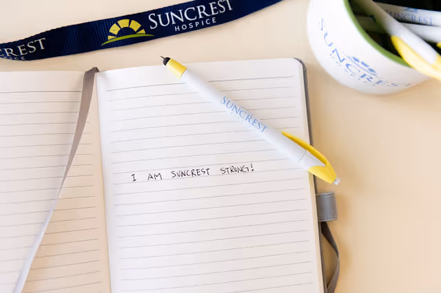 Open notebook displays the handwritten slogan 'I AM SUNCREST STRONG!' beside a yellow pen and lanyard.