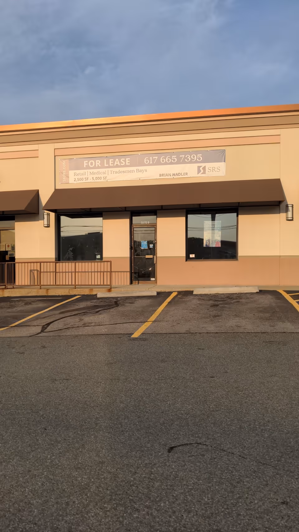 Front view of a commercial building with a For Lease banner and parking lot.