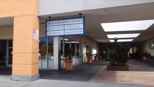 Exterior corridor of a building with a Senior Helpers sign and potted plants.