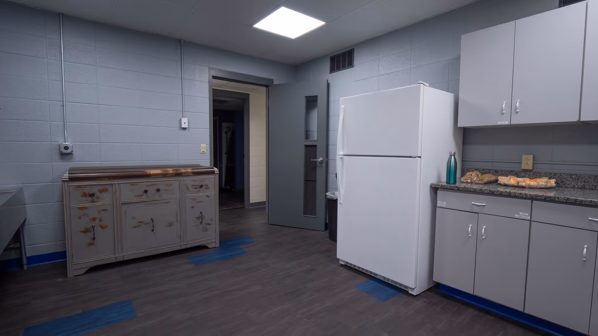 Industrial kitchen area with a white refrigerator, gray cabinets, and a rustic sideboard.
